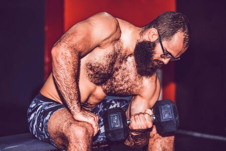 Bearded muscular man working out with dumbbells weights at the gymの写真素材