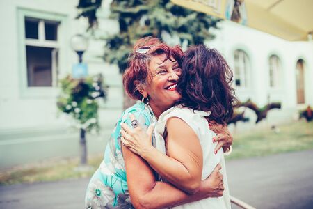 Close-up photo of two emotional happy senior female friends hugging each other outdoorsの写真素材