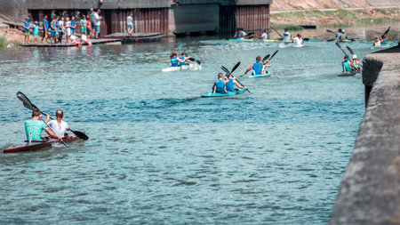 Team of a young man and woman athlete on rowing kayak on lake during competition. Followers watch a...