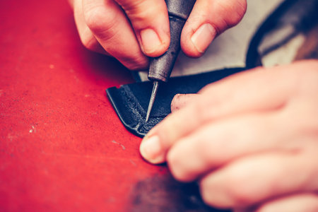 Close up of a shoemaker hands working with leather using crafting tools
