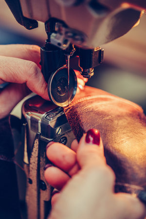 Hands of an experienced seamstress stitching a part of the shoe  in the handmade footwear industry