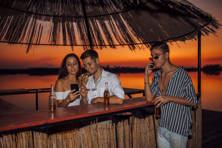 Young smiling couple relaxing and watching something on smart phone in the beach  bar, while their...