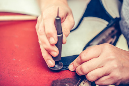 Close up of a male shoemaker working with leather using crafting tools. Process of making leather...