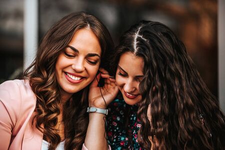 Image of a two pretty happy cheerful  women - friends using mobile phone listening music with earphones.の写真素材
