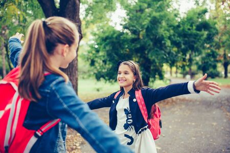 Two school friends hugging, meet in the park. Walking into each other with open arms and smiling. The concept of school, study, education, friendship, childhoodの写真素材