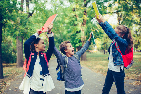 Back to school. Close up three happy friends with backpacks laughing and having fun in the park. Boy...