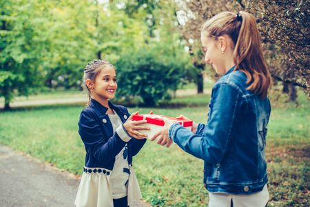 Happy little girl giving gift in a red box to her friend. People, children, holidays, friends and friendship conceptの写真素材