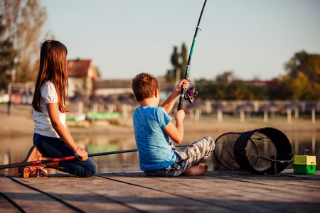 Two young cute little friends, boy and girl fishing on a lake in a sunny summer day. Kids are playing. Friendship.の写真素材