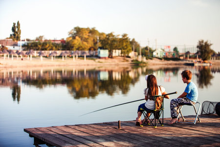 Two young cute little friends, boy and girl fishing on a lake in a sunny summer day. Kids are playing. Friendship.Selective focusの写真素材
