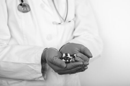 Doctor in white medical coat and sterile gloves holding many different pills. Black and white photo.の写真素材