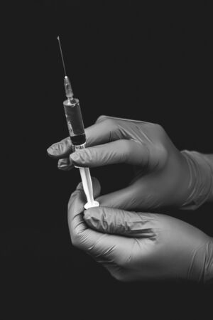 Medical syringe close-up, the doctor in sterile gloves to do the injection and vaccination on black background. Black and white photo.の写真素材