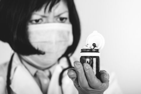 Doctor in sterile gloves and medical mask holding many different pills. Black and white photo.の写真素材