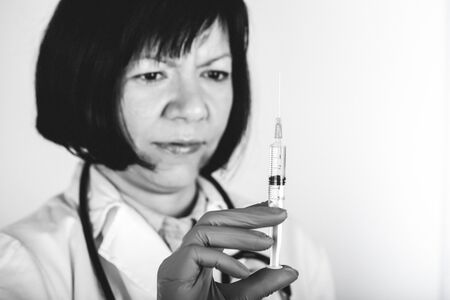 Female doctor in white lab coat on white background holds a syringe with medicine in his hand, an injection. Black and white photo.の写真素材