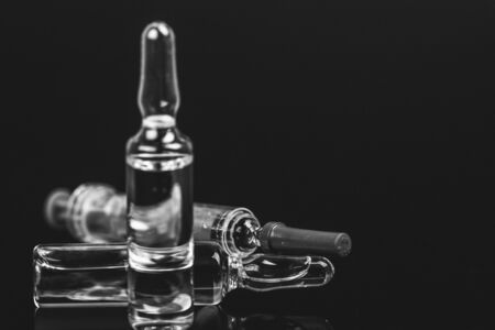 Sterile medical vials with medication solution, ampoules, and syringe isolated on a black background. Black and white photo.の写真素材