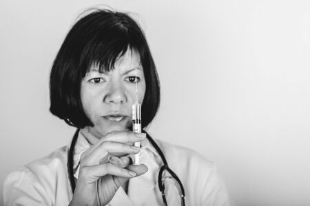 Female doctor in white lab coat on white background holds a syringe with medicine in his hand, an injection. Black and white photo.の写真素材