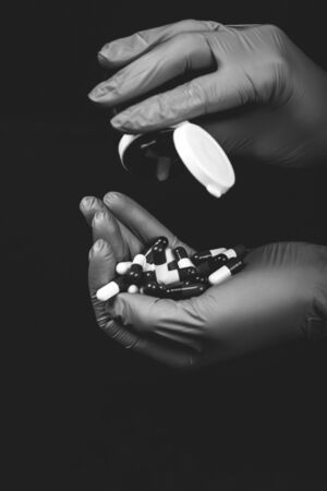 Female hands in sterile gloves holding a lot of different capsules and pills isolated on black background. Black and white photo.の写真素材