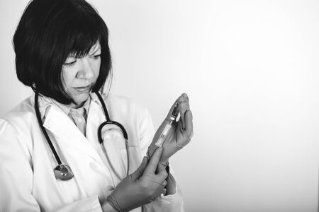 Female doctor in white lab coat on white background holds a syringe with medicine in his hand, an injection. Black and white photo.の写真素材