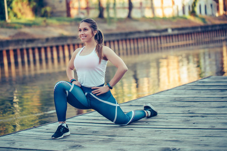 Young beautiful woman doing stretching exercises tor her legs, by the river.