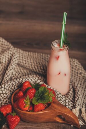 Strawberry smoothie or milkshake in jar with fresh strawberries in wooden bowl on rustic background, healthy food for breakfast and snackの写真素材
