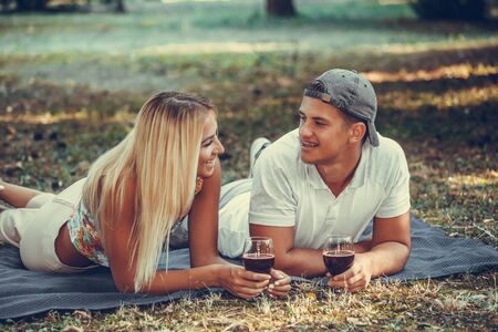 Beautiful  young couple talking, flirting and enjoying a glass of wine on a romantic picnic in a parkの写真素材