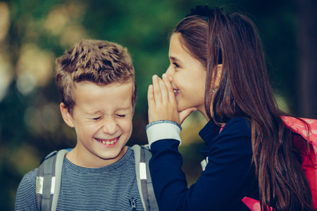 Close up two happy friends with backpacks laughing and having fun in the park. A small girl...