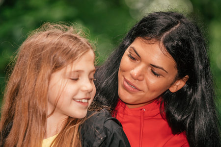 Beautiful mother and her cute daughter sitting in forest talking and having fun together, spending good time in spring nature.の写真素材