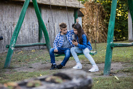 Happy smiling kids watching video on  smartphone, while sitting on swingの写真素材