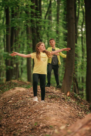 Enjoying the beutiful nature. Little boy and girl with raised arms  walking and enjoying the fresh air in green forest. Selective focus.の写真素材