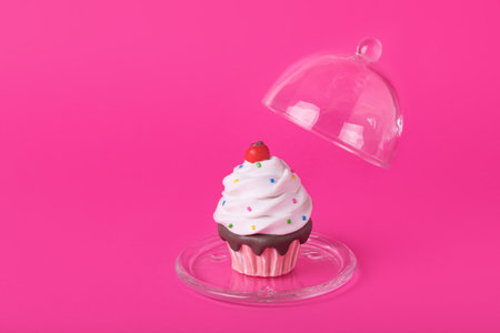 Colorful cupcake with colorful sugar decoration under glass cover on pink  background. Creative minimal artwork. Copy spaceの写真素材