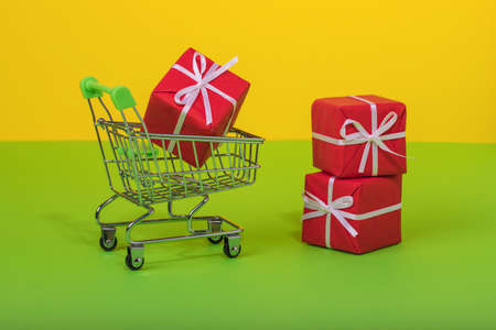 Shopping cart full of gift box on green and illuminating yellow color background.  Minimal concept idea. Shop trolley at supermarket. Sale, discount, shopaholism concept. Consumer society trend.の写真素材