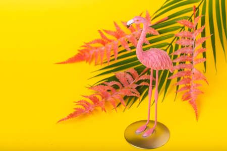 Trendy Summer idea made with pink flamingo figure with tropical leaves on bright illuminating yellow background. Minimal summer concept. Copy spaceの写真素材