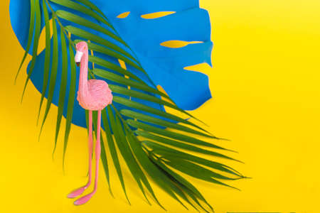 Trendy Summer idea made with pink flamingo figure and different tropical plant on bright illuminating yellow background. Minimal summer party concept.の写真素材