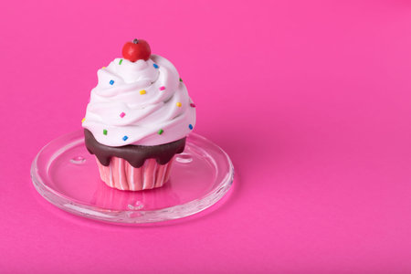 Creative minimal concept made of cupcake with colorful sugar decoration on a glass plate on pink ...