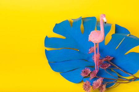 Trendy Summer idea made with pink flamingo figure with blue monstera leaf on bright illuminating yellow background. Minimal summer party concept. Copy spaceの写真素材