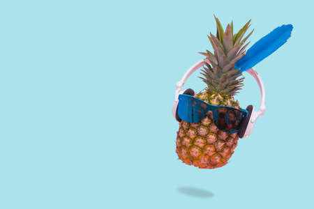 Creative trendy summer invitation card with pineapple wearing sunglasses and headphones on pastel blue background . Minimal scene of fun, party, fashion, trend and funny art design.Copy spaceの写真素材
