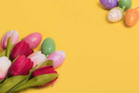 Creative Easter border composition made of colorful eggs and tulips on illuminating yellow background. Minimal easter concept. Easter card with copy space for text.の写真素材