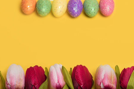 Creative Easter frame made of colorful eggs and tulips on illuminating yellow background. Minimal...