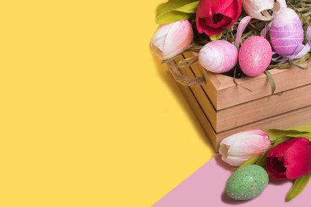 Easter colored eggs in a basket and tulips on a trendy illuminating yellow background. Minimal...