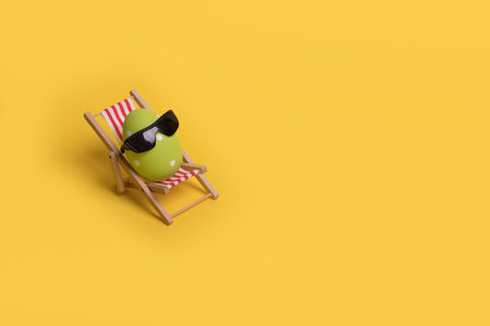 Minimal  funny composition with Easter egg with sunglasses while sitting on deck chair on illuminating yellow background. Creative idea of spring or summer vacation, holiday and travel concept. Free space for textの写真素材
