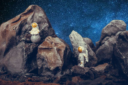 Astronauts with gold visor and White Spacesuit on rock surface with space background. First astronaut on the moon sitting and meditating while second astronaut walking.の写真素材