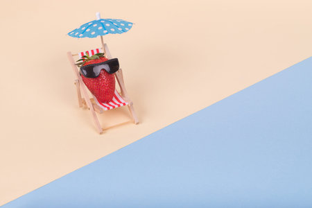 Creative  idea made of deck chair, sun umbrella and strawberry with sunglasses on a beach. Minimal ...