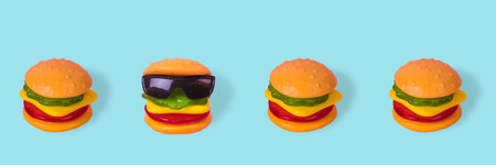 Creative idea made from a hamburger with sunglasses that is placed in a row with normal burgers. Minimal funny food concept. Be different. Minimal junk food concept. Abstract creative food concept with gummy candiesの写真素材