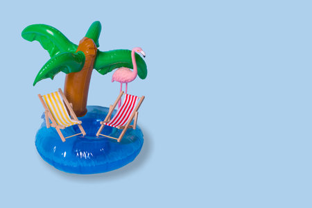 Creative summer idea with inflatable palm ring, deck chairs and exotic flamingo bird on pastel blue background. Minimal travel concept. Summertime color mood. Copy space.の写真素材