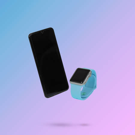 Mobile phone and smart watch while levitating in the air on a background illuminated by a blue and pink color gradient. Creative minimal background. Pop art, conceptual art.の写真素材