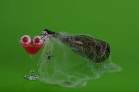 Bottle with cobweb and red bloody cocktail with eyeballs on a green background. Minimal Halloween concept.の写真素材