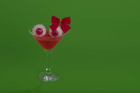 Red bloody cocktail with eyeballs and bow ribbon on a green background. Minimal Halloween concept.の写真素材