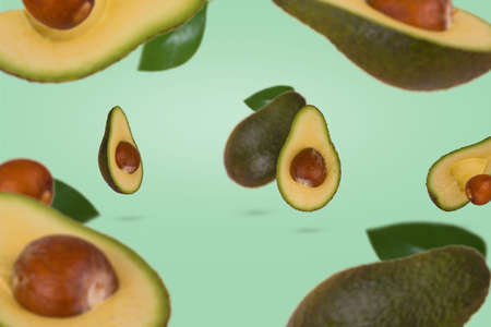 Fresh ripe whole and sliced avocado flying in air isolated on green background. Healthy food, diet, tropical exotic fruit, trendy food product. Creative and minimal food concept.の写真素材