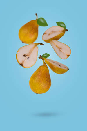 Fresh ripe whole and sliced pears flying in air isolated on a blue background. Creative and minimal food concept.の写真素材