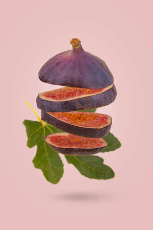 Fresh ripe sliced fig floating  in air isolated on pastel pink background. Creative food concept. Vegetarian diet idea.の写真素材