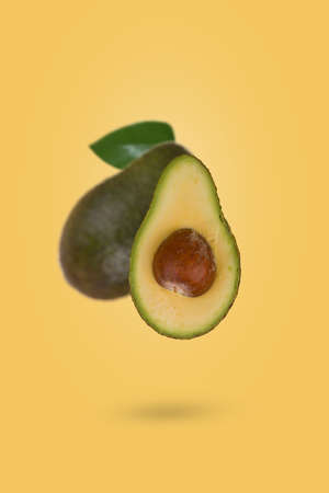 Fresh ripe whole and sliced avocado flying in air isolated on yellow background. Healthy food, diet, tropical exotic fruit, trendy food product. Creative and minimal food concept.の写真素材
